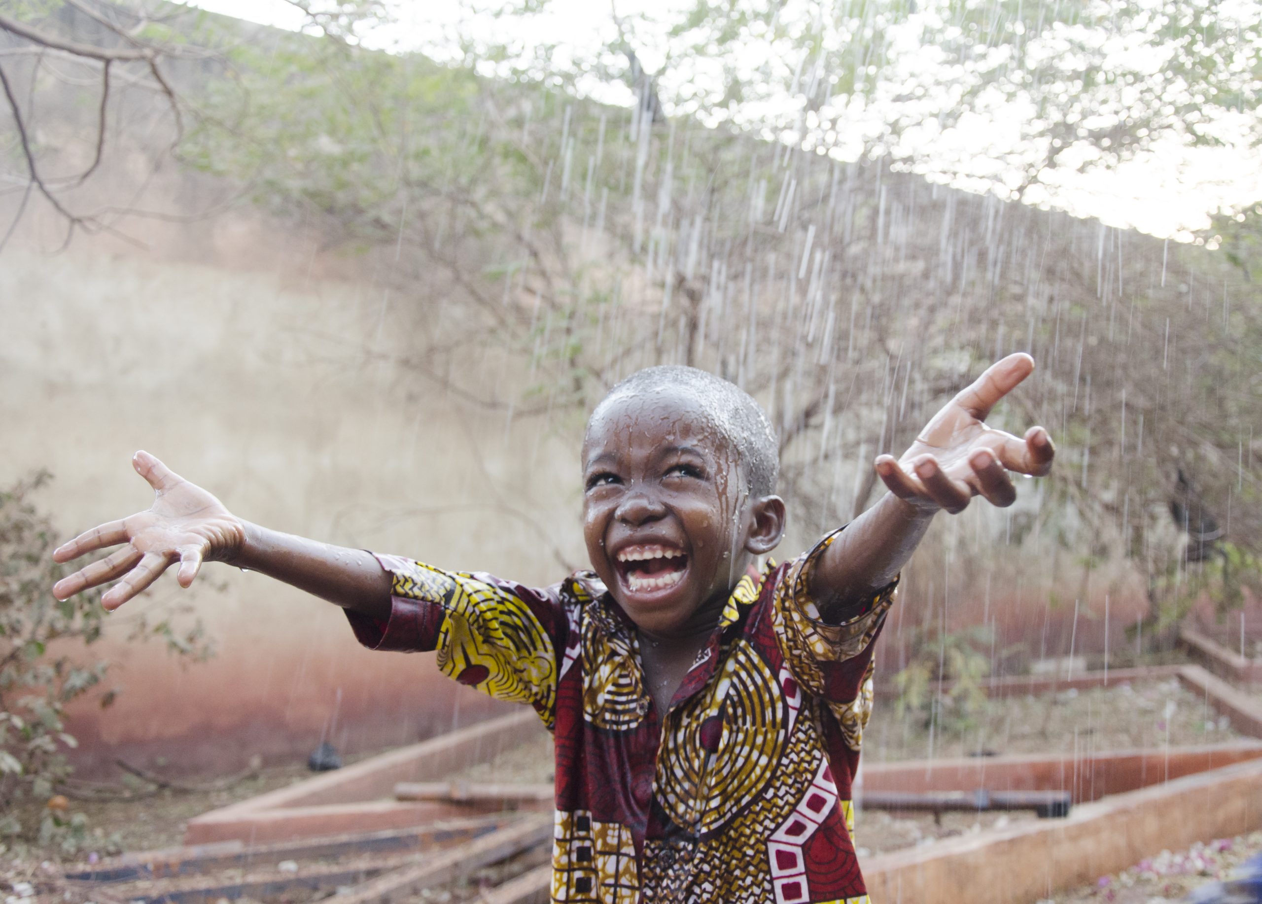 Little African boy outdoors happy to get some rain, water for Africa symbol and concept - handsome sweet child posing outdoors.
